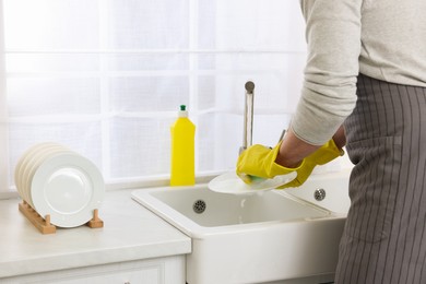 Man washing plate above sink in kitchen, closeup