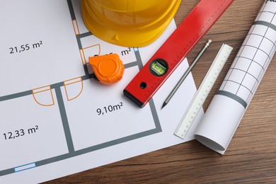 Construction drawings, safety hat, tape measure and bubble level on wooden table, flat lay