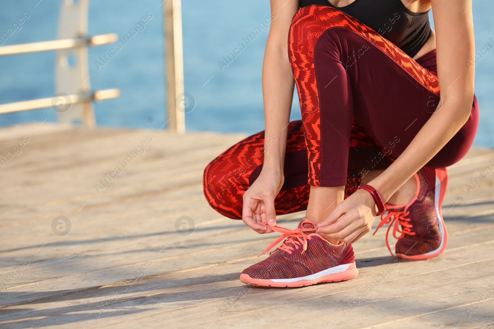 Photo of Young woman tying shoelaces on pier. Morning workout