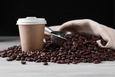Photo of Coffee to go. Paper cup, roasted beans and scoop on light table