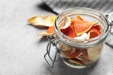 Photo of Glass jar with dry orange peels on light gray textured table, space for text