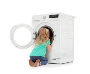Photo of Cute little girl looking into washing machine with laundry on white background