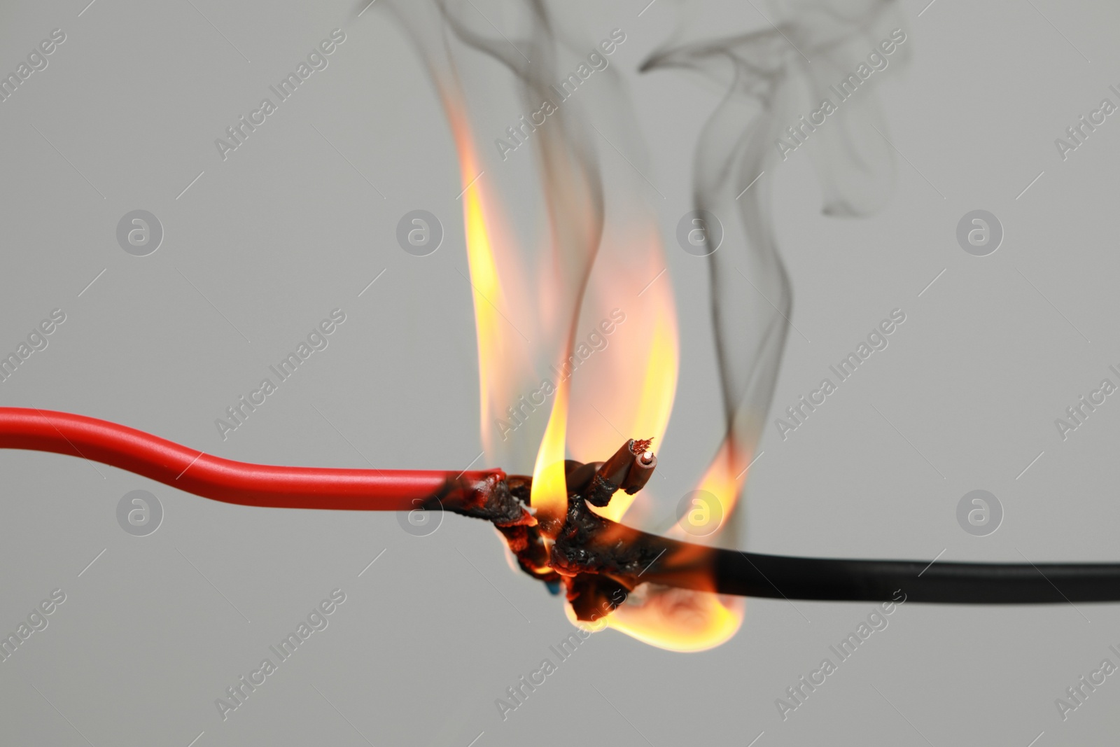 Photo of Inflamed red wire on grey background, closeup. Electrical short circuit