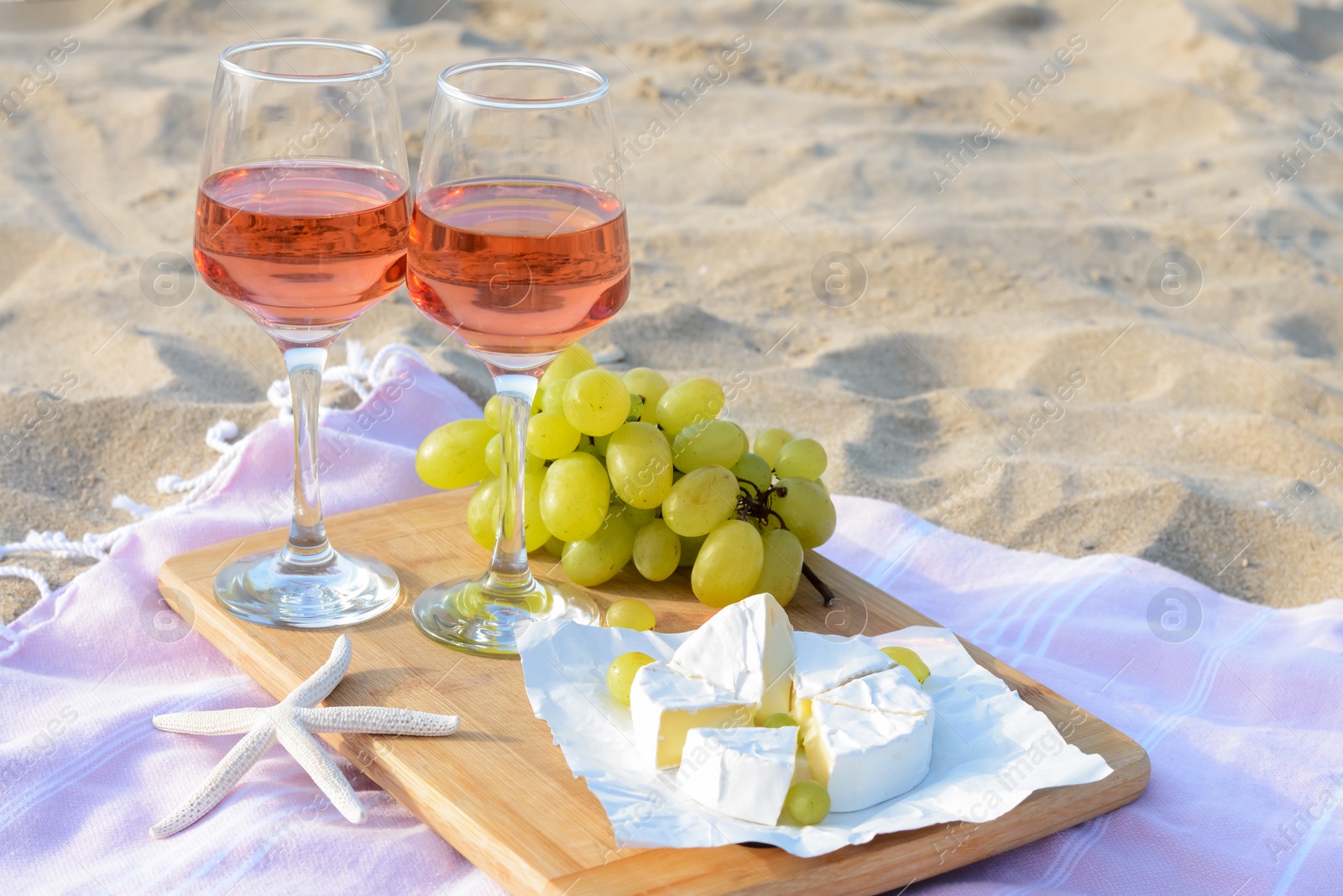 Photo of Glasses with rose wine and snacks for beach picnic on sand outdoors