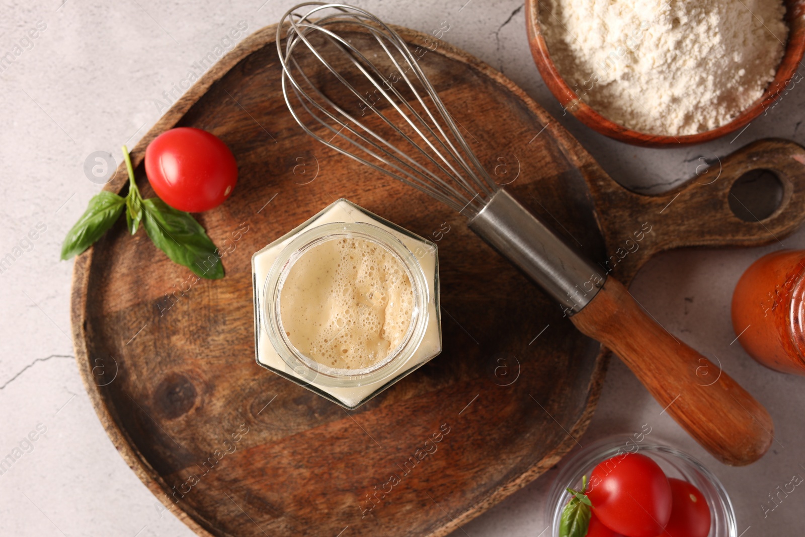 Photo of Pizza dough starter in glass jar, products and whisk on gray textured table, flat lay