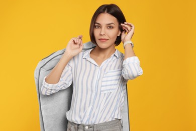Photo of Woman holding garment cover with clothes on yellow background. Dry-cleaning service
