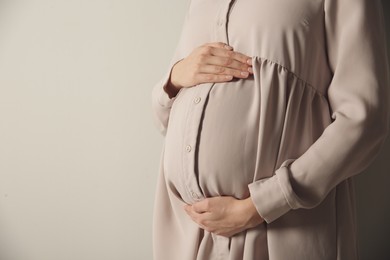 Pregnant woman touching her belly on light grey background, closeup. Space for text