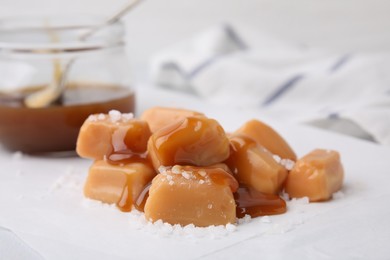 Yummy caramel candies and sea salt on white table, closeup