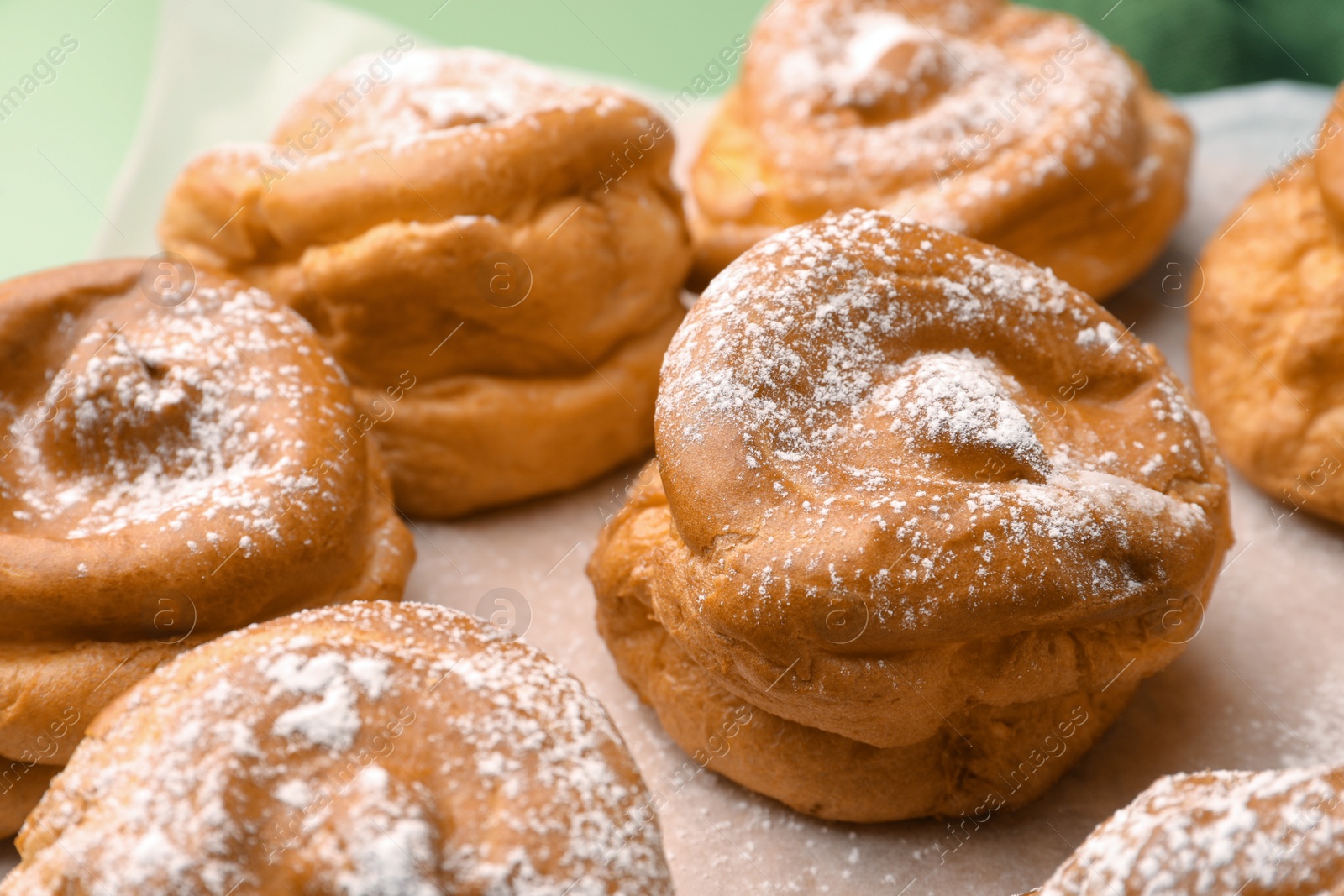 Photo of Delicious profiteroles with powdered sugar on parchment paper, closeup