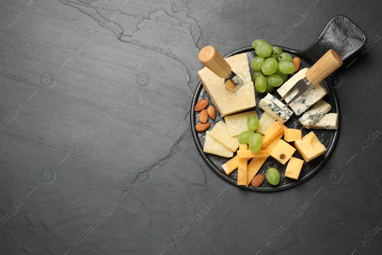 Photo of Cheese platter with specialized knife and fork on black table, top view. Space for text