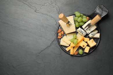 Photo of Cheese platter with specialized knife and fork on black table, top view. Space for text
