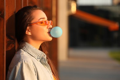 Photo of Beautiful young woman in sunglasses blowing bubble gum outdoors. Space for text