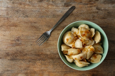 Photo of Delicious cooked dumplings with fried onion on wooden table, flat lay. Space for text