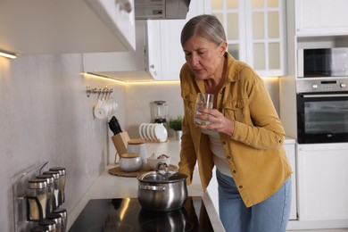 Menopause. Woman with glass of water suffering from hot flash in kitchen