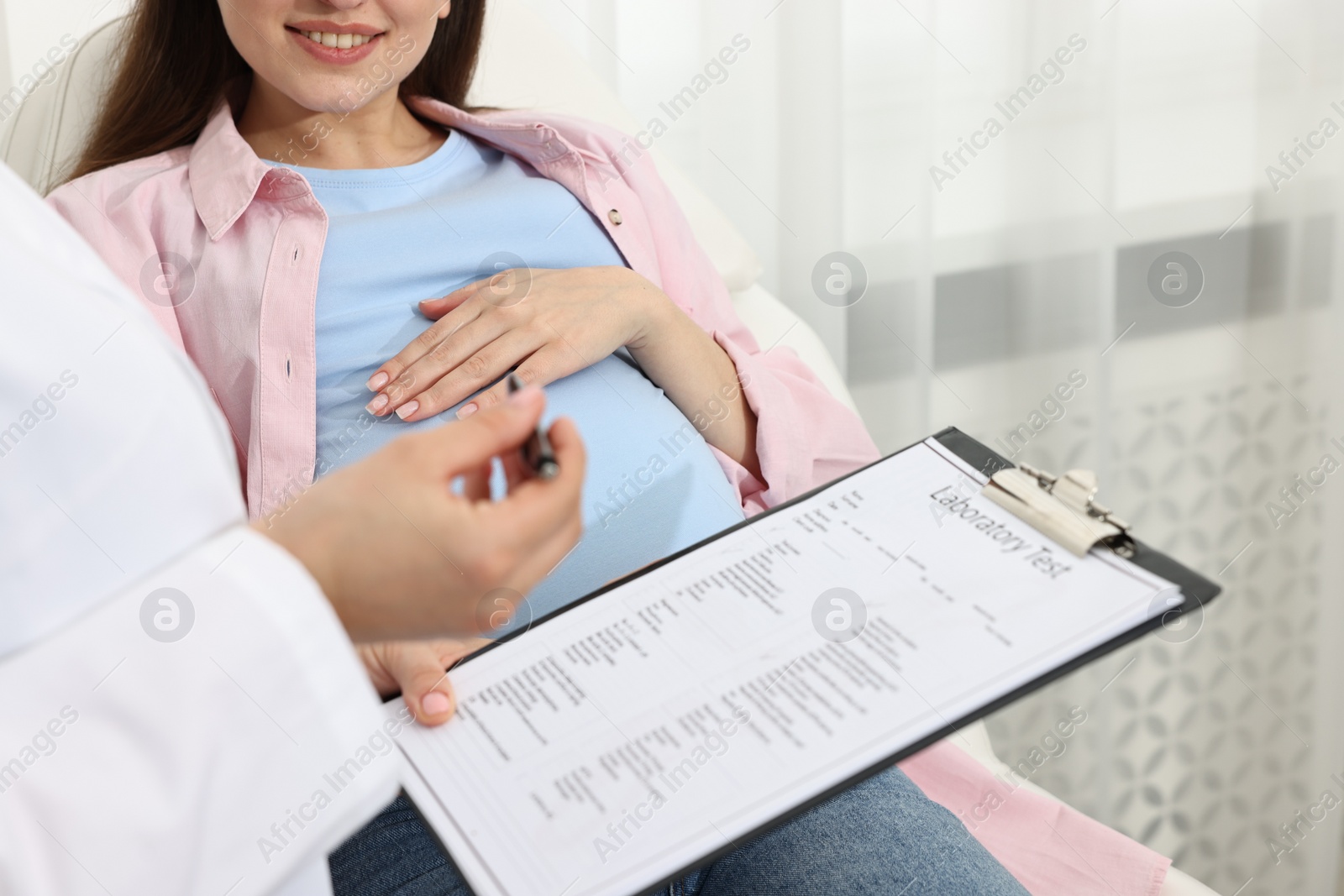 Photo of Doctor with results of laboratory test consulting smiling pregnant patient in clinic, closeup