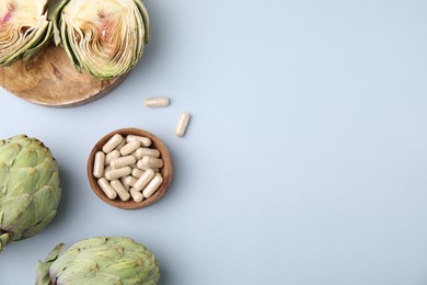 Photo of Bowl with pills and fresh artichokes on light grey background, flat lay. Space for text