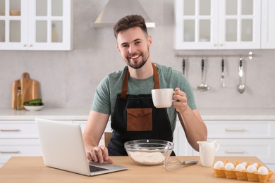 Photo of Portrait of man with baking ingredients and laptop at table in kitchen. Time for hobby