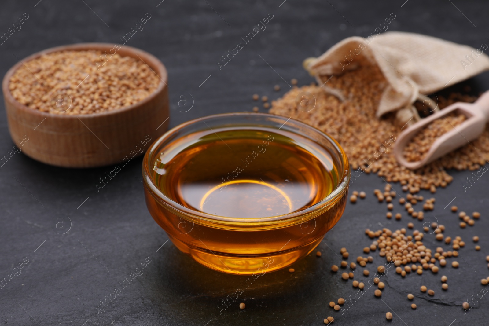 Bowl with natural oil and mustard seeds on black table Photo of Bowl with natural oil and mustard seeds on black table
