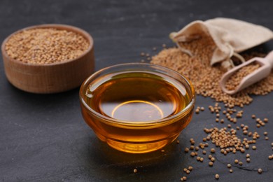 Photo of Bowl with natural oil and mustard seeds on black table