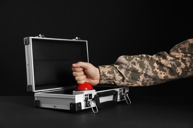 Photo of Serviceman pressing red button of nuclear weapon at black table, closeup. War concept