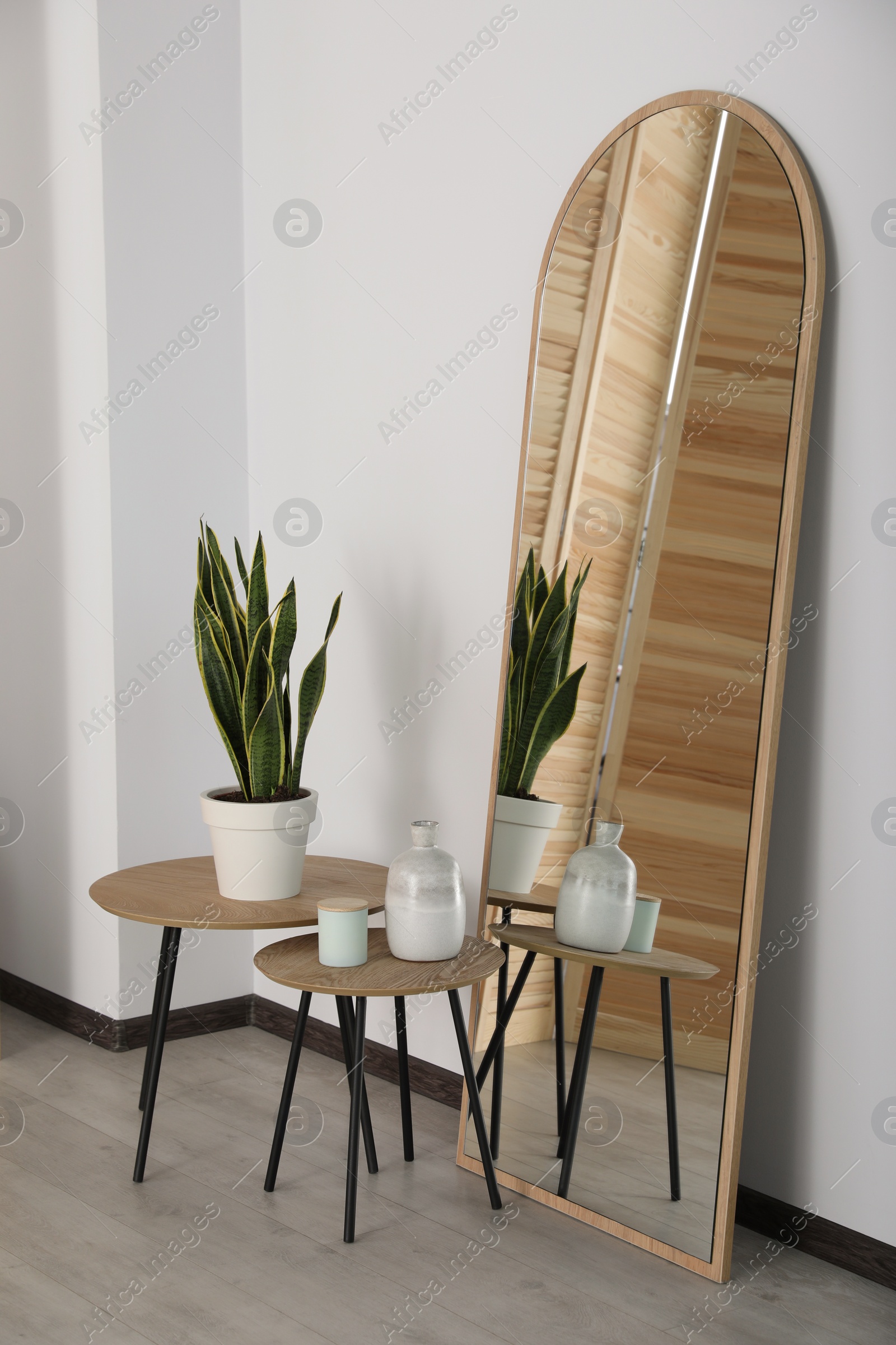 Photo of Leaning floor mirror near nesting tables with houseplant and decor in room