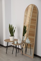 Photo of Leaning floor mirror near nesting tables with houseplant and decor in room