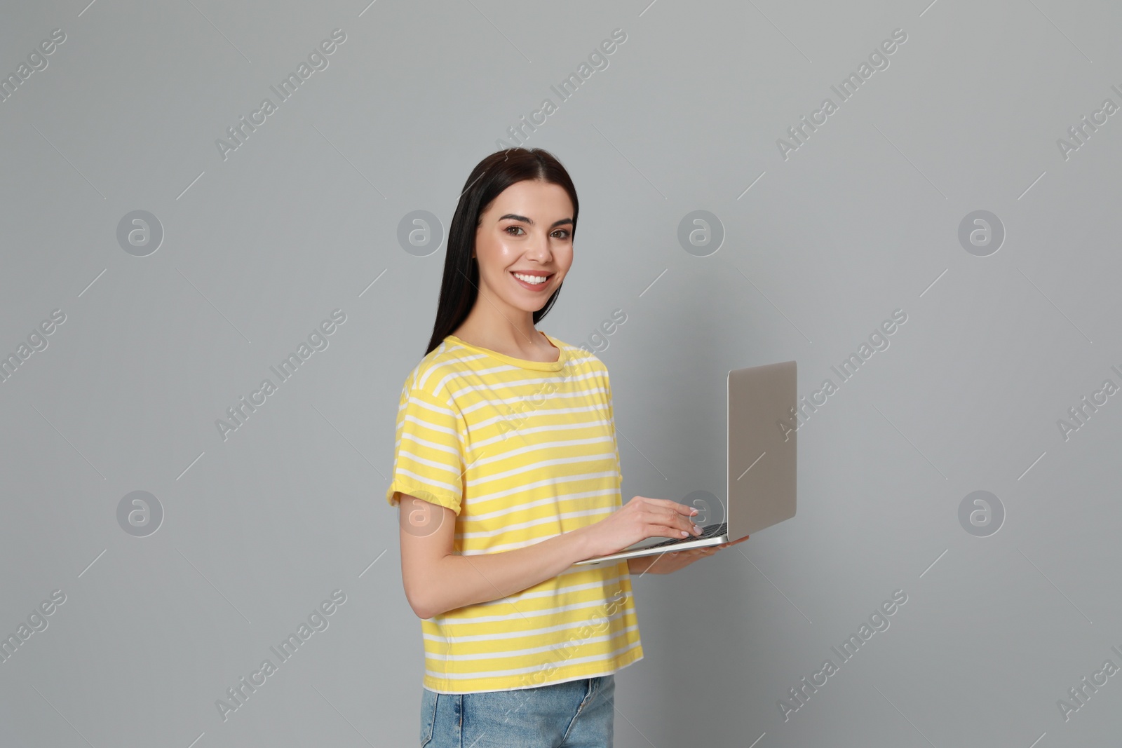 Photo of Young woman with modern laptop on light grey background