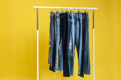 Photo of Rack with different jeans on yellow background