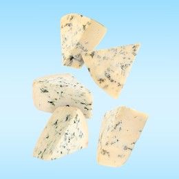 Image of Pieces of tasty cheese falling on light blue background