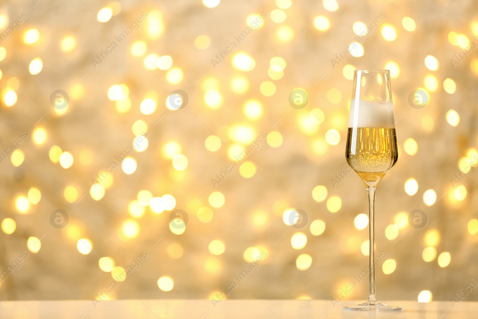 Photo of Glass of champagne on table against blurred lights. Space for text