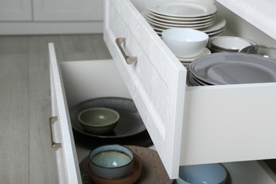 Photo of Open drawers with different plates and bowls in kitchen, closeup