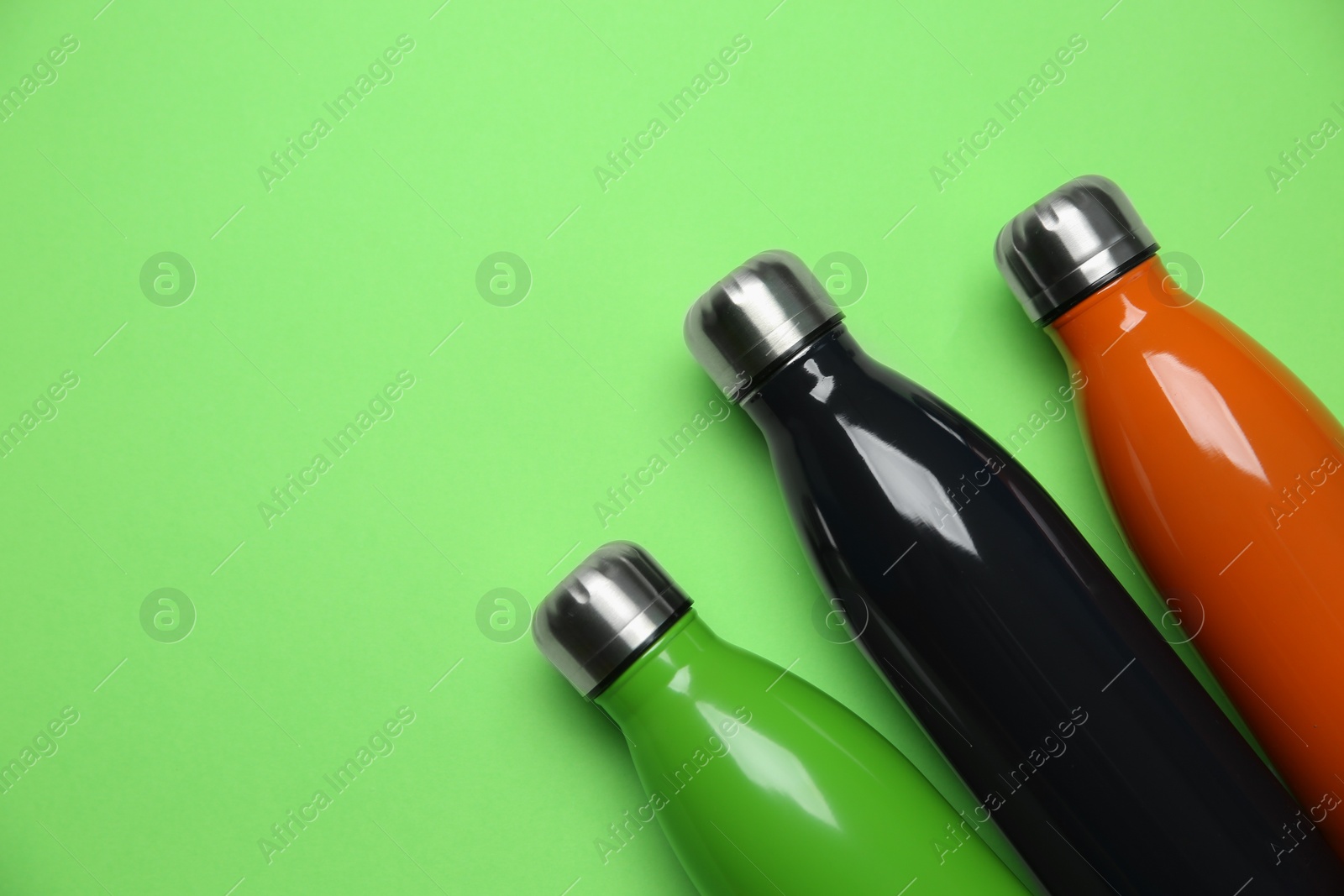 Photo of Different thermo bottles on green background, flat lay. Space for text