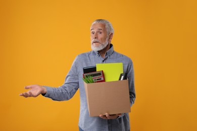 Photo of Confused unemployed senior man with box of personal office belongings on orange background