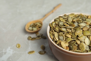 Photo of Bowl of raw pumpkin seeds on light grey marble table, closeup. Space for text