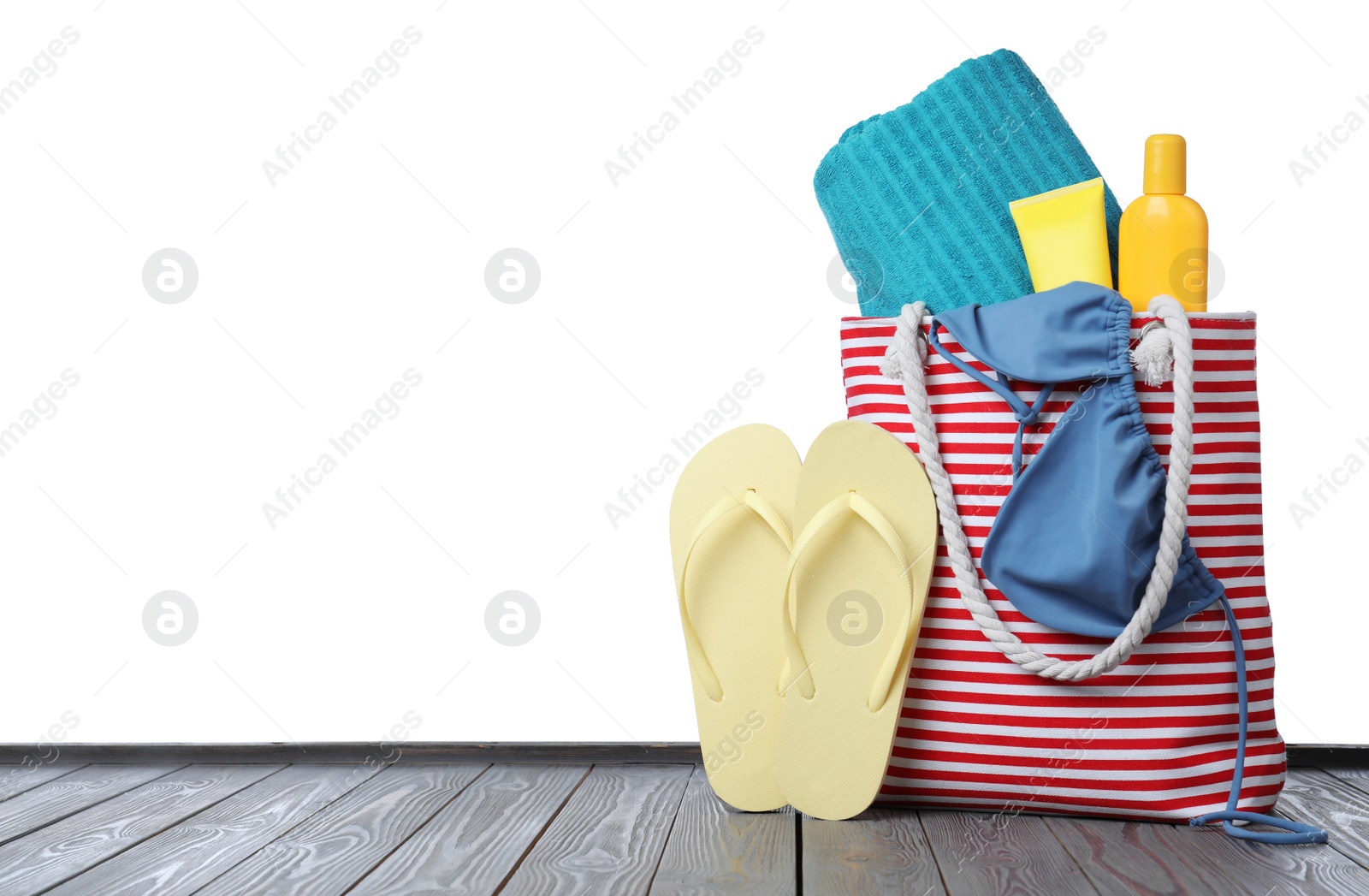 Photo of Stylish bag with beach accessories on grey wooden table against white background