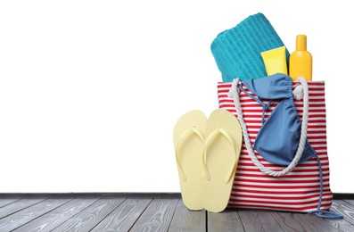 Stylish bag with beach accessories on grey wooden table against white background