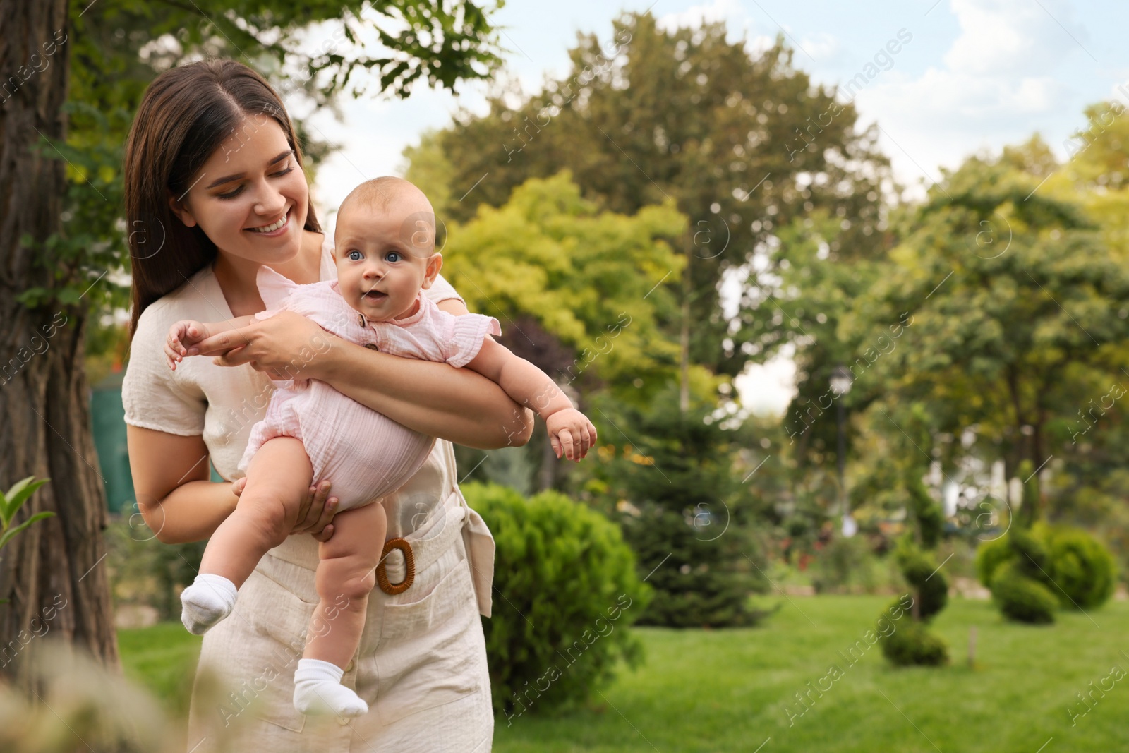 Photo of Happy mother with adorable baby walking in park on sunny day, space for text