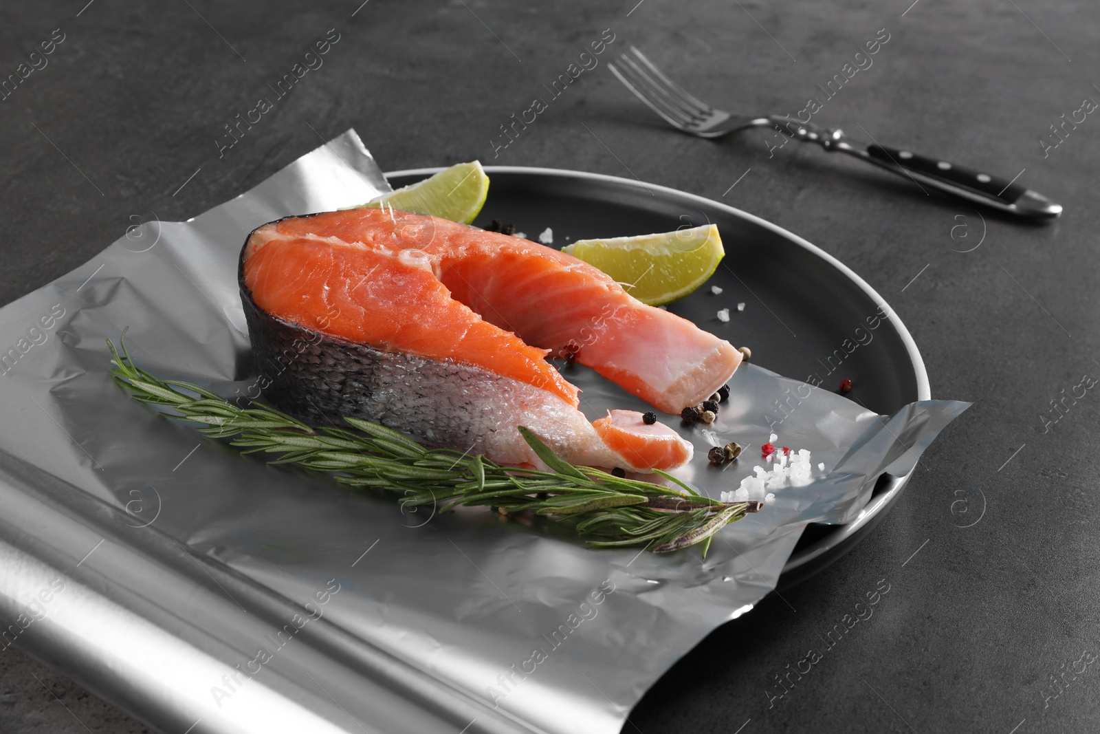 Photo of Aluminum foil with raw fish, lime, rosemary and spices on grey table. Baking salmon