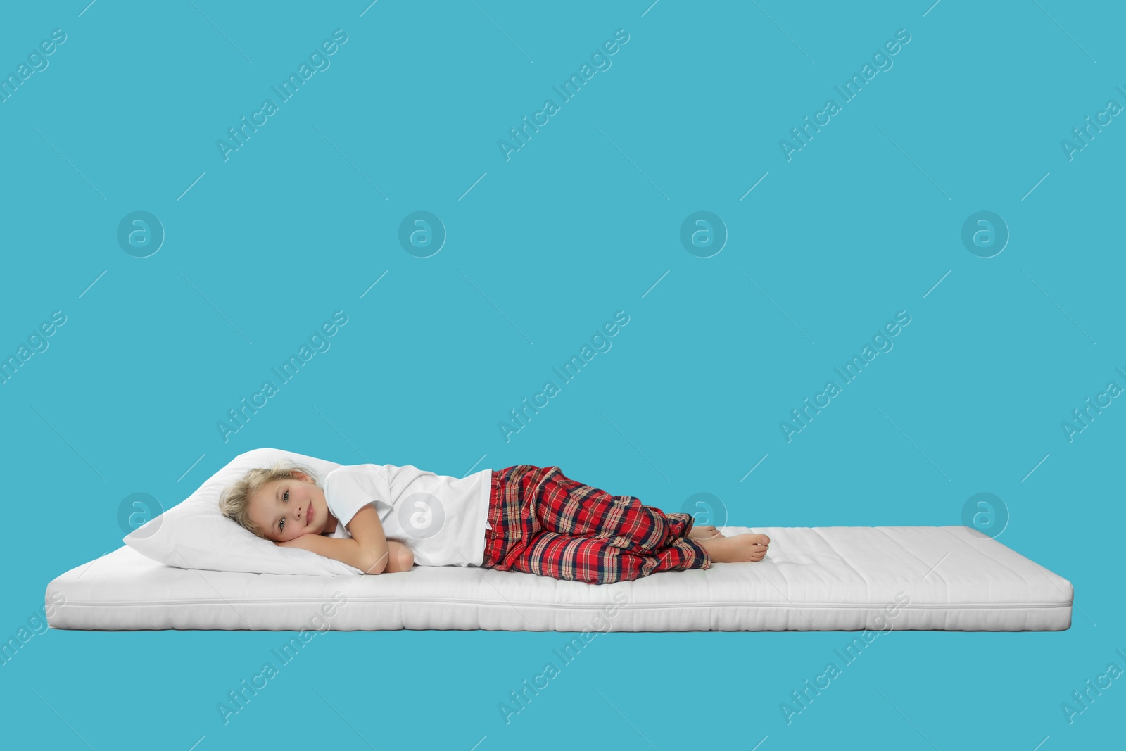 Photo of Little girl lying on comfortable mattress against light blue background, space for text