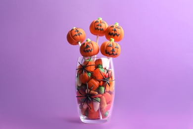 Photo of Delicious pumpkin shaped cake pops on violet background. Halloween treat