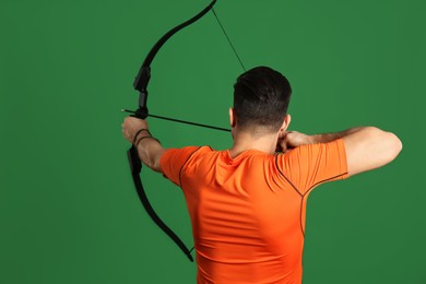 Man with bow and arrow practicing archery on green background, back view