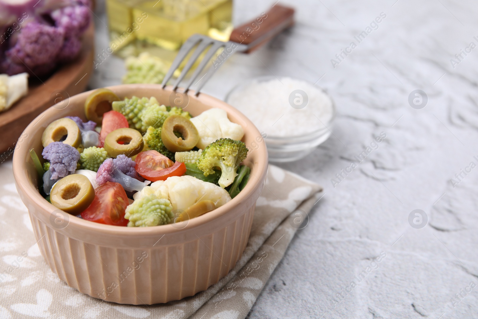 Photo of Delicious salad with cauliflower, tomato and olives served on white textured table, closeup. Space for text