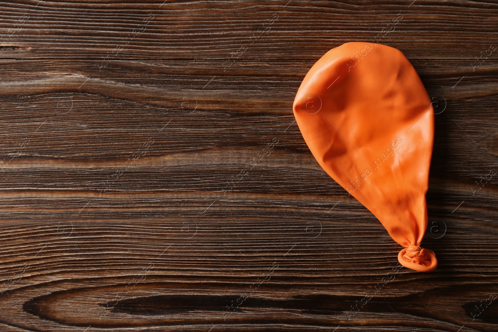 Photo of Orange deflated balloon on wooden background, top view with space for text