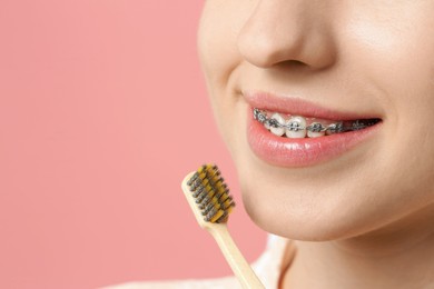 Smiling woman with dental braces and toothbrush on pink background, closeup. Space for text