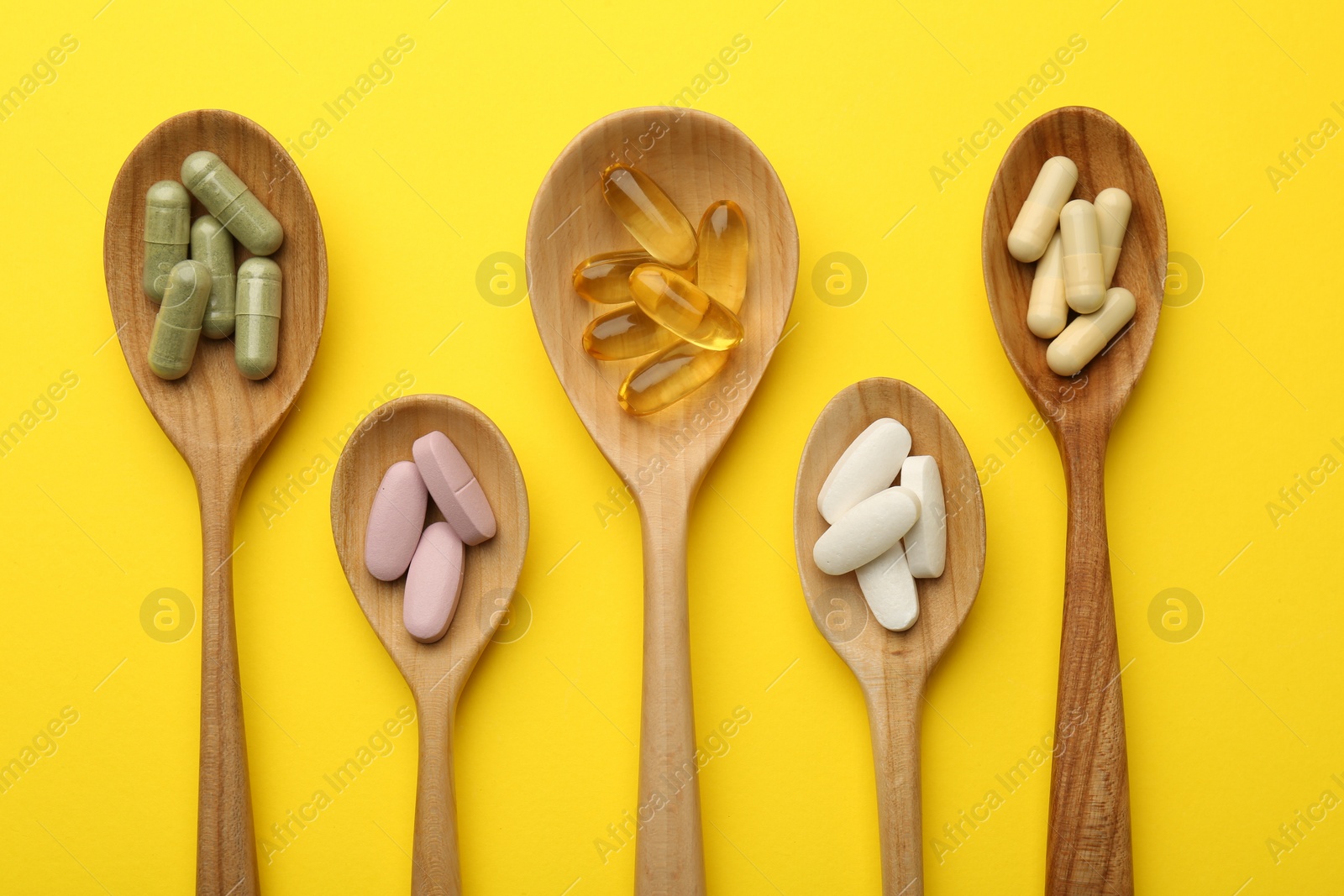 Photo of Different vitamin pills in spoons on yellow background, flat lay