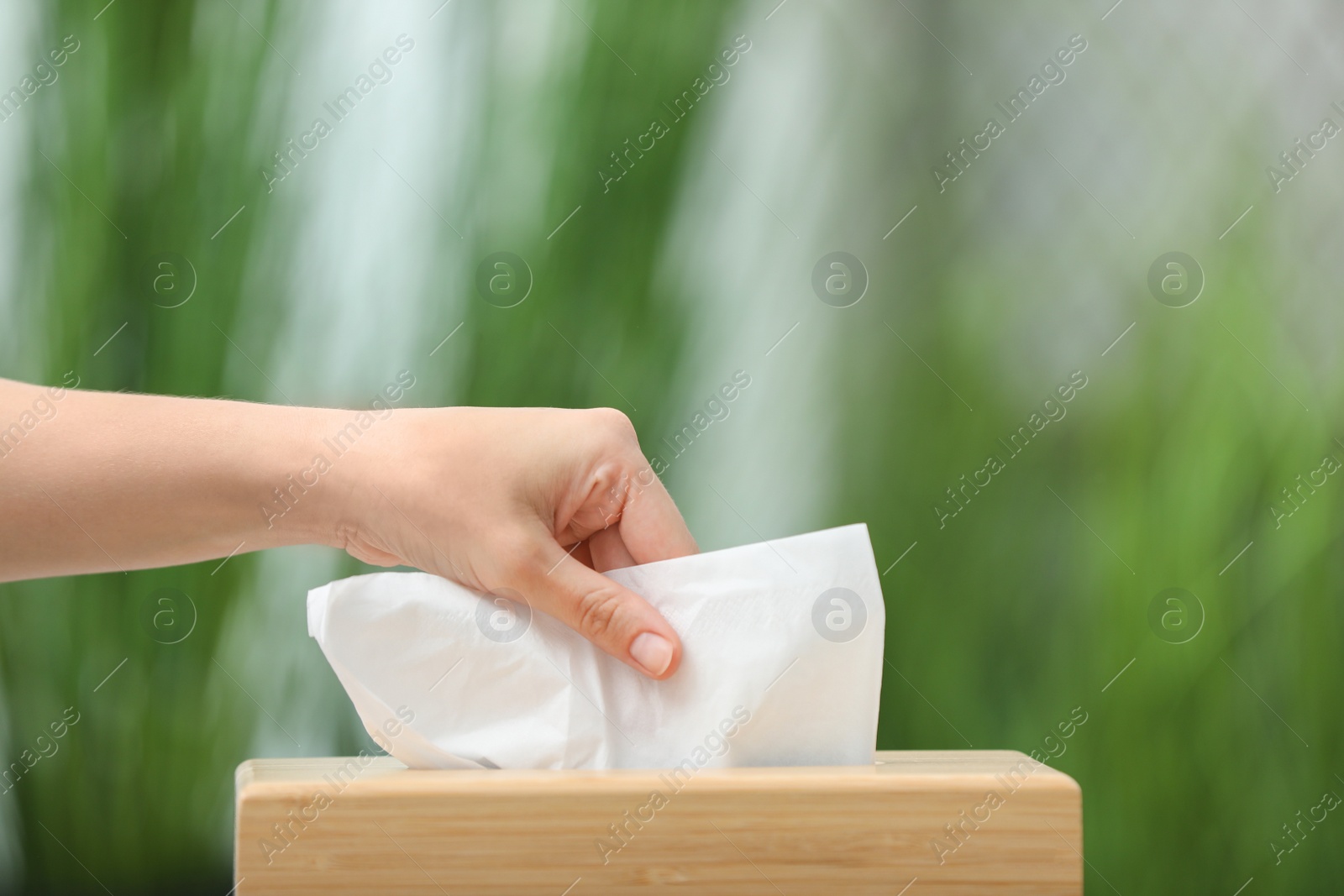 Photo of Woman taking paper tissue from holder on blurred background, closeup