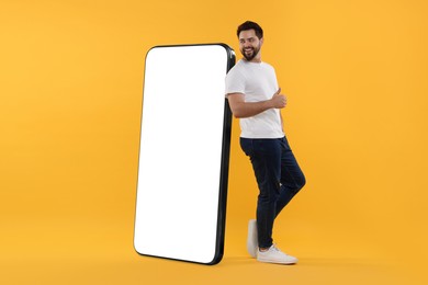 Image of Man standing near huge mobile phone with empty screen on dark beige background. Mockup for design