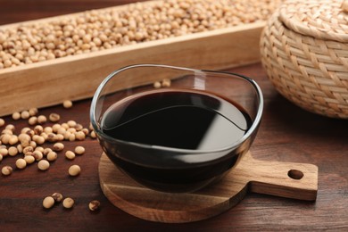 Soy sauce in bowl and soybeans on wooden table