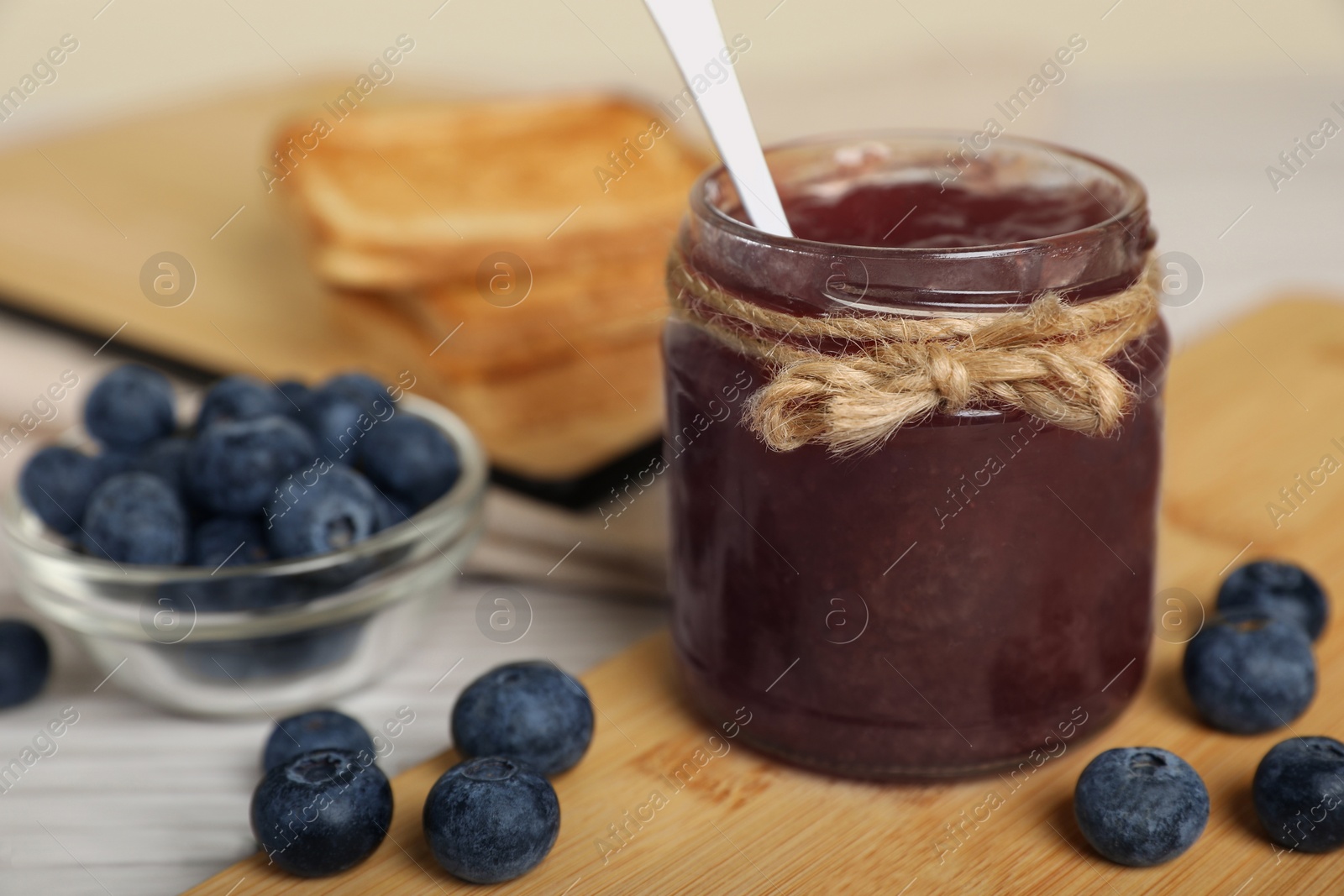 Photo of Jar of delicious blueberry jam and fresh berries on white wooden table, closeup. Space for text