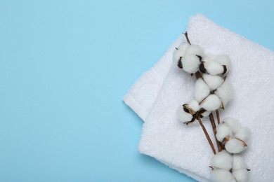 Photo of White terry towel and cotton flowers on light blue background, top view. Space for text